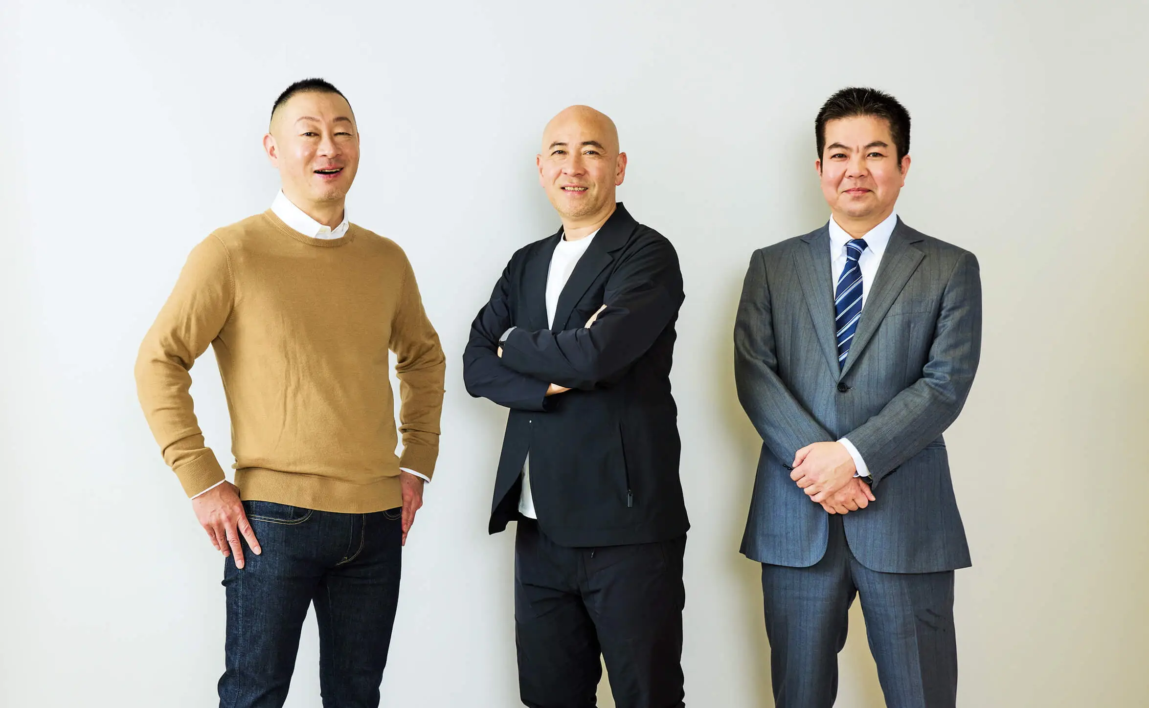 白いシャツを着た三人の男性と黒いジャケットを着た一人の男性が並んで笑顔で立っている様子。